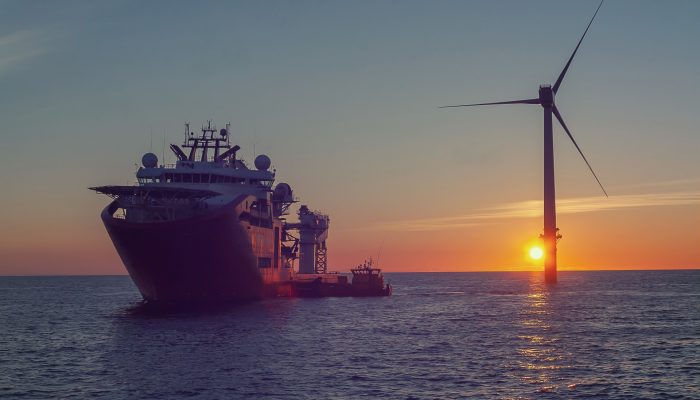 Service operational vessel, with crew transfer vessel alongside and sun setting on wind turbine
